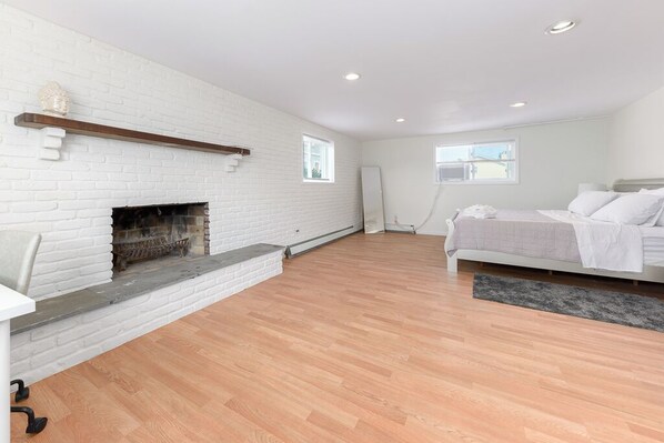A bedroom with a white brick fireplace, a bed with white bedding, and a large window.