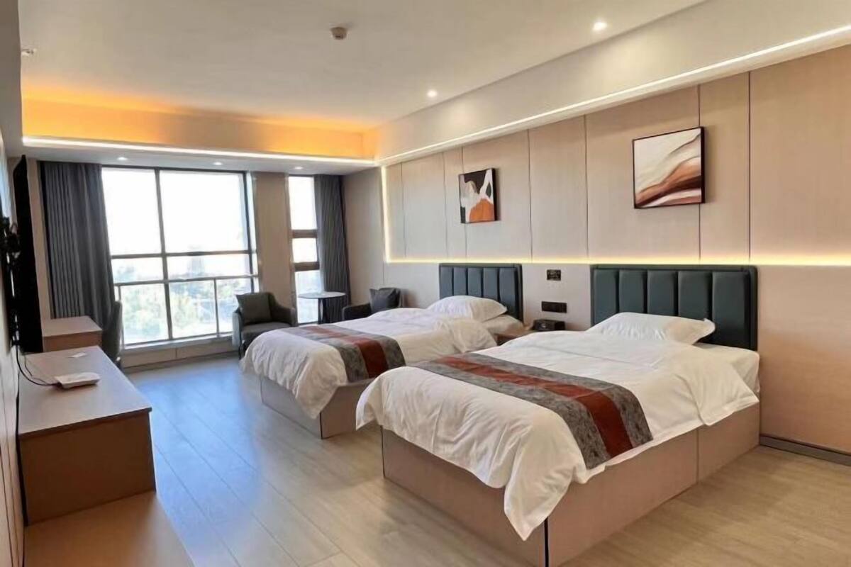 A hotel room with two beds, a desk, and a large window.