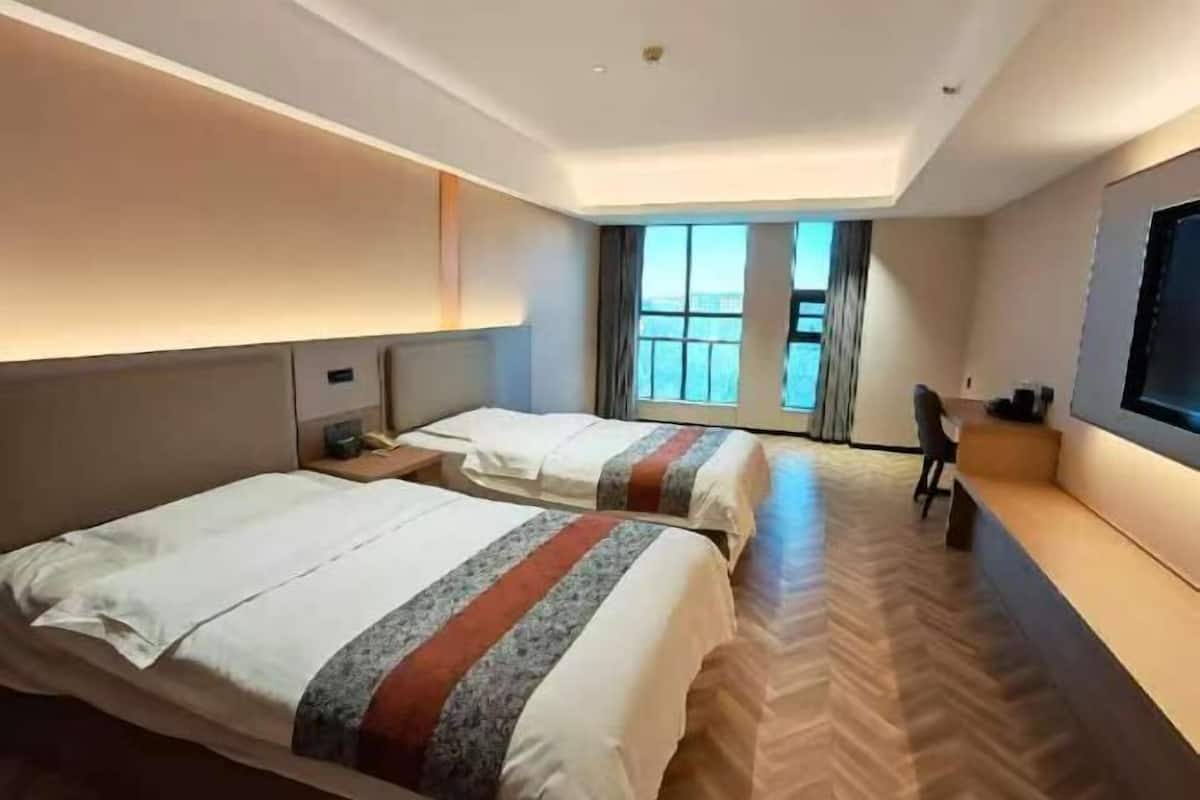 A hotel room with two beds, a TV, a desk, and a view of the city.