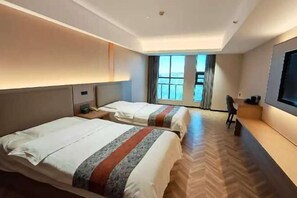 A hotel room with two beds, a TV, a desk, and a view of the city. - Oulian International Hotel (Erenhot)