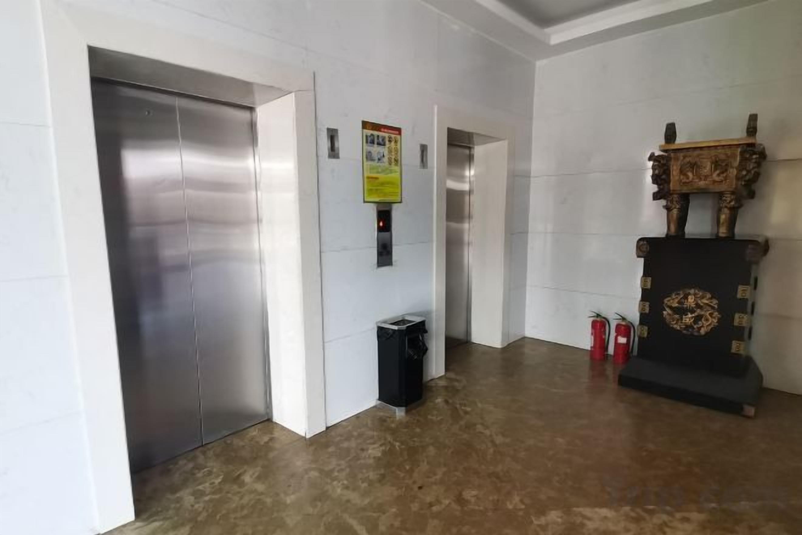 A hallway with an elevator, a trash bin, and a decorative wooden structure.