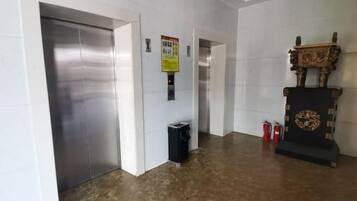 A hallway with an elevator, a trash bin, and a decorative wooden structure.