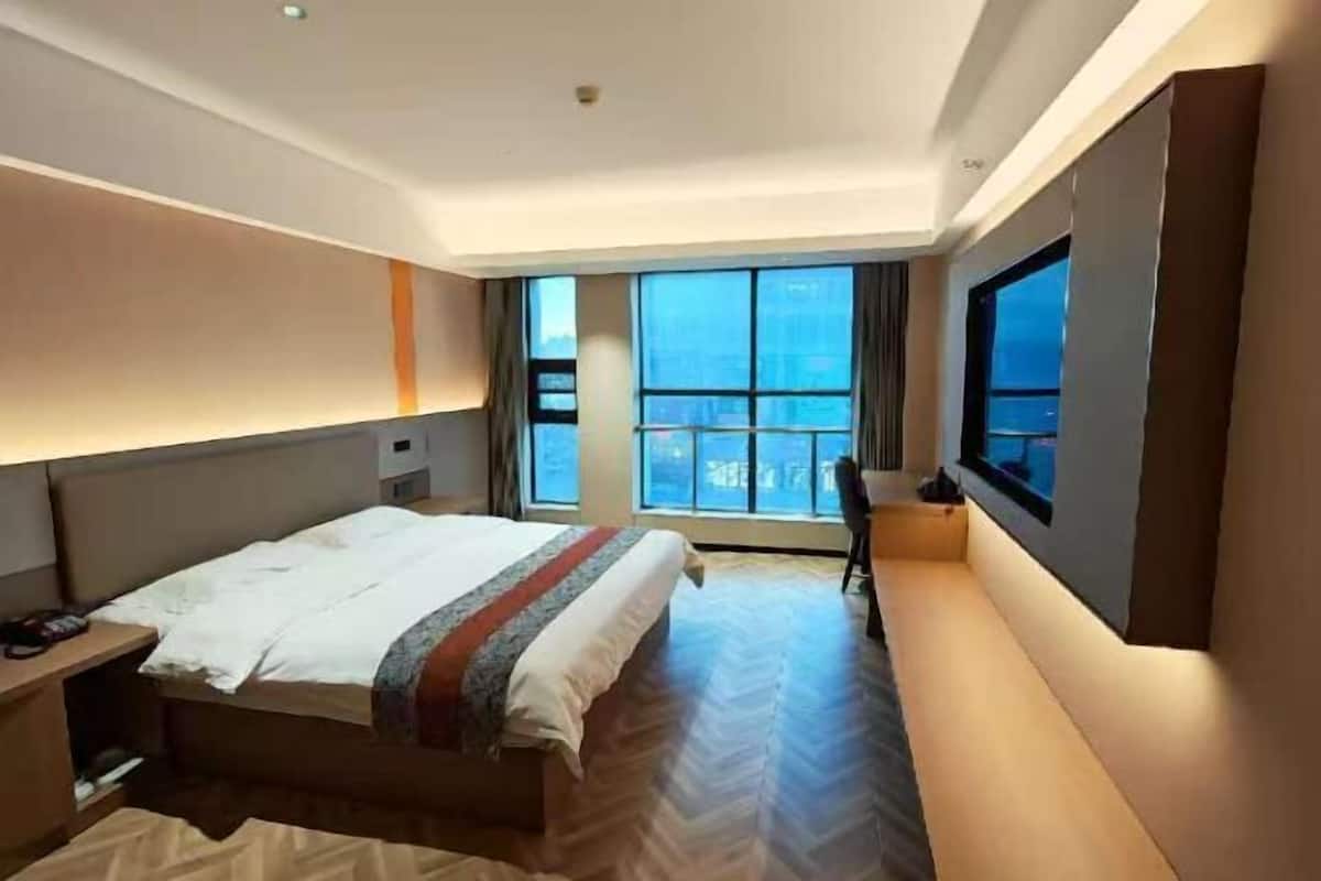 A hotel room with a large bed, a desk, a chair, a TV, and a window with a view.