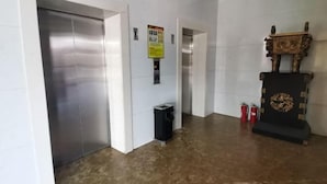 Un pasillo con un ascensor metálico, un bote de basura y dos extintores.