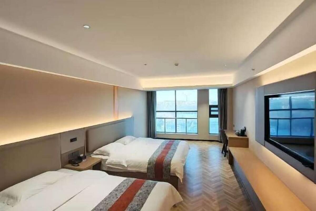 A hotel room with two beds, a large window, a TV, and a desk.