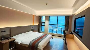 Habitación de hotel con cama, mesita de noche, silla y un amplio ventanal con vistas.
