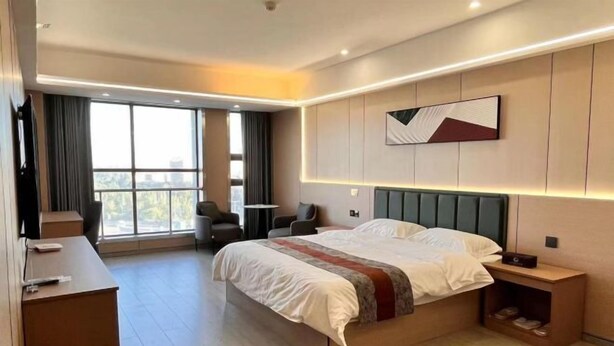Un hotel moderno con una cama grande, un escritorio, una silla y vistas de la ciudad a través de amplias ventanas.