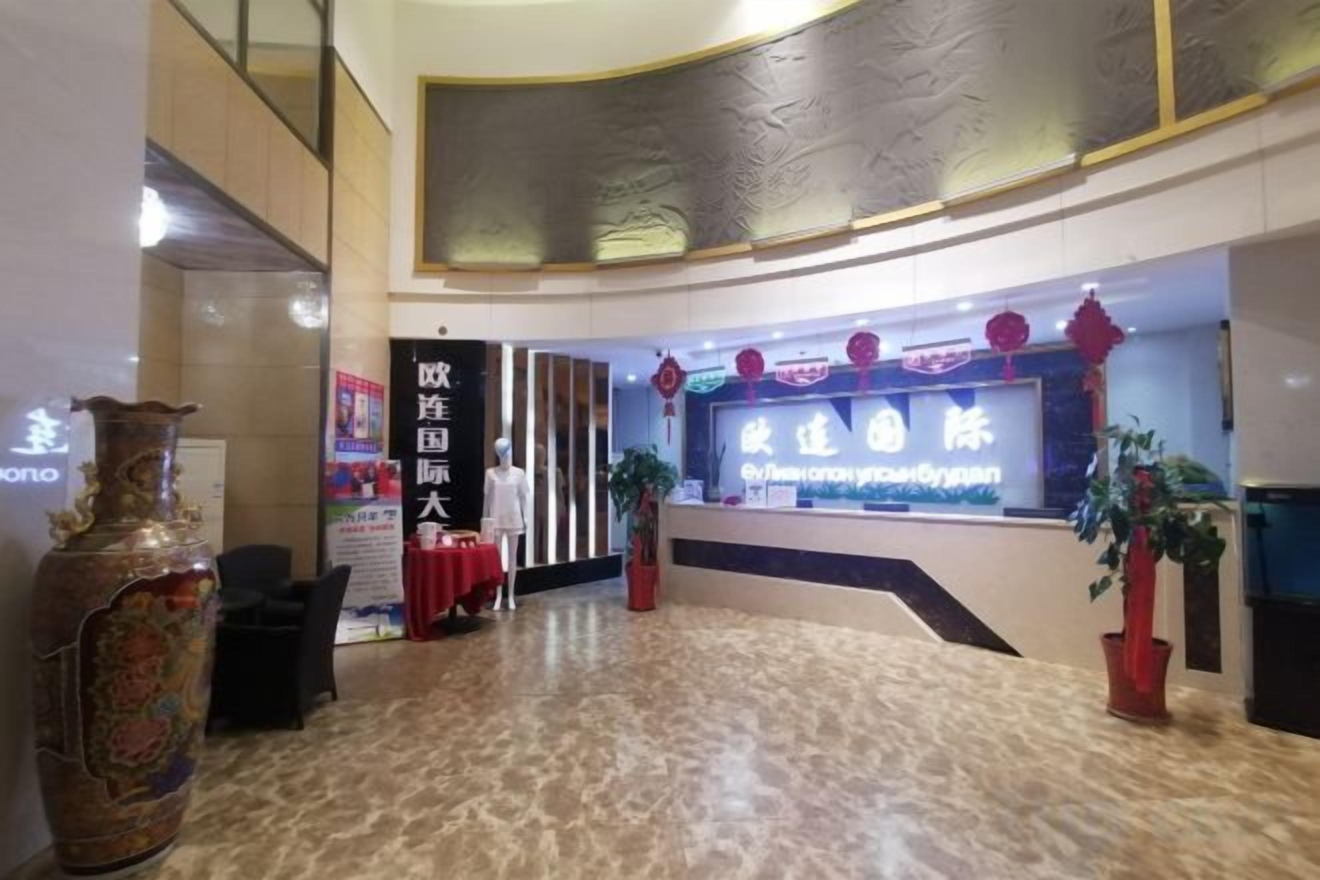Een hotel lobby met een receptiebalie, een grote vaas en een spandoek.