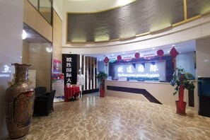 A hotel lobby with a reception desk, a large vase, and a banner.