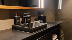 A modern bathroom with a black countertop, a black sink, and a mirror above it. - Studio Apartment in CBD (Newcastle)
