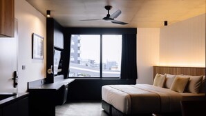 A hotel room with a bed, desk, and a large window offering a city view.