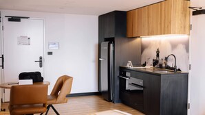 A compact kitchen with a refrigerator, sink, and wooden cabinets. There's a small dining area with a chair and a table.