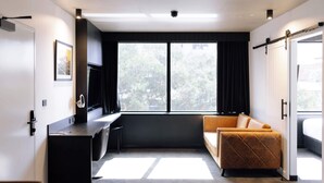 Una habitación de hotel moderna con escritorio, sofá y ventana grande con cortinas.