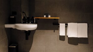 A bathroom with a white sink, black fixtures, a wooden shelf with toiletries, and two white towels hanging on a rack. - One Bedroom Accessible In CBD (Newcastle)