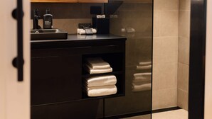 Une salle de bain moderne avec une paroi en verre, un meuble-lavabo noir, un miroir et des serviettes soigneusement pliées.