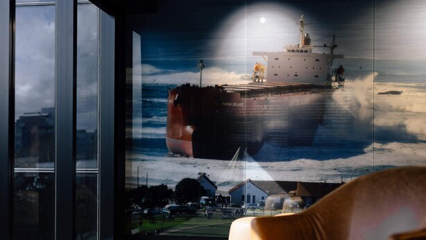 A room with a large window, a brown leather sofa, a glass coffee table, and a wall mural of a ship. - Two Bedroom Interconnect In CBD (Newcastle)