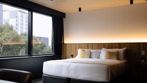 A modern hotel room with a large bed, a desk, and a window offering a view of buildings and trees. - Two Bedroom Interconnect Deluxe In CBD (Newcastle)