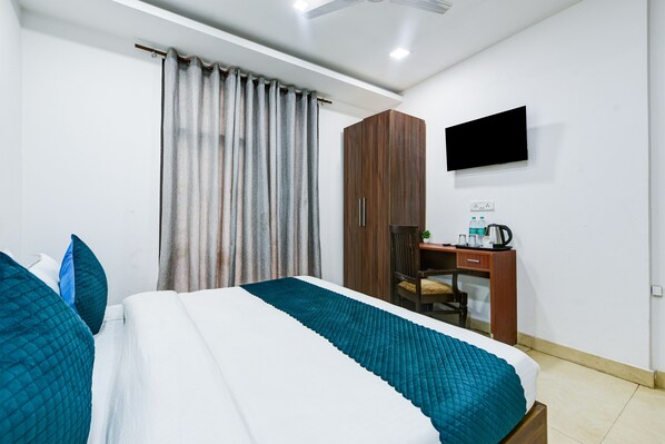A hotel room with a bed, curtains, a desk, a chair, and a television.
