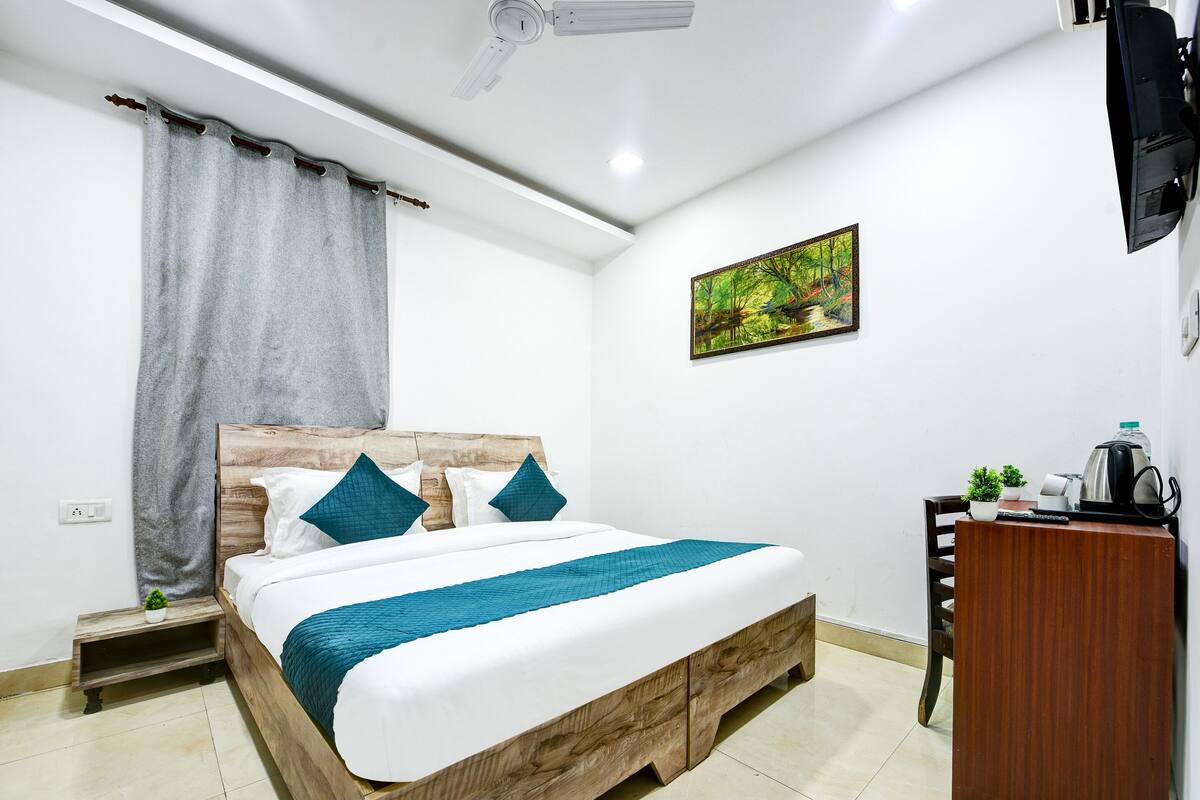 Un dormitorio ordenado con cama, escritorio, silla, televisor y un cuadro en la pared.