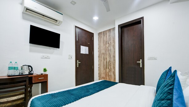 Een hotelkamer met een bed, een bureau met stoel, een airconditioner en twee deuren.
