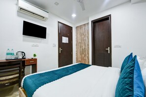 A hotel room with a bed, a desk with a chair, an air conditioner, and two doors.