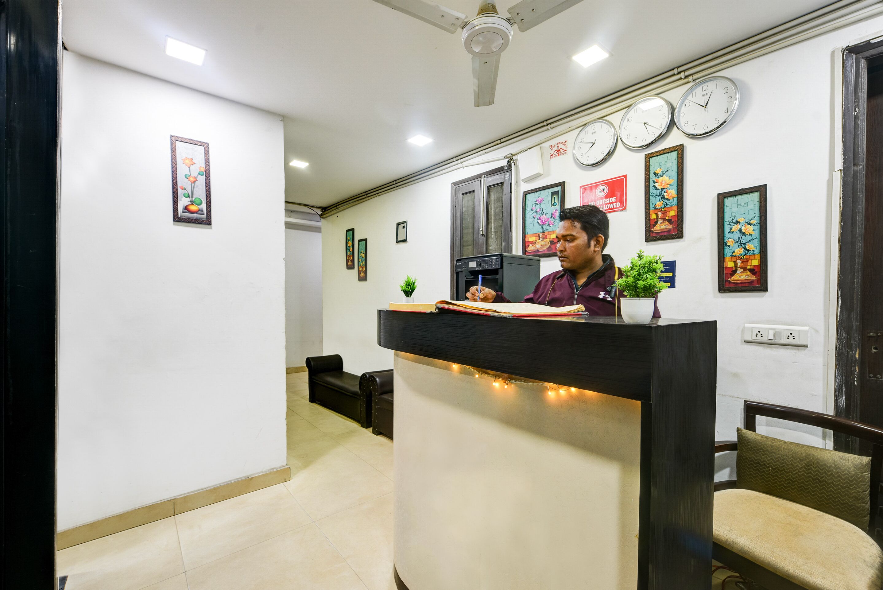 A reception desk with a person seated behind it, a ceiling fan, and several clocks on the wall.