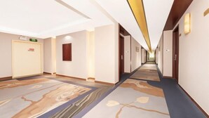 Corredor de hotel com carpete estampado, portas e sinalização de saída de emergência.