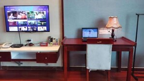 Quarto de hotel com escrivaninha, televisão exibindo um serviço de streaming, laptop, luminária e telefone.