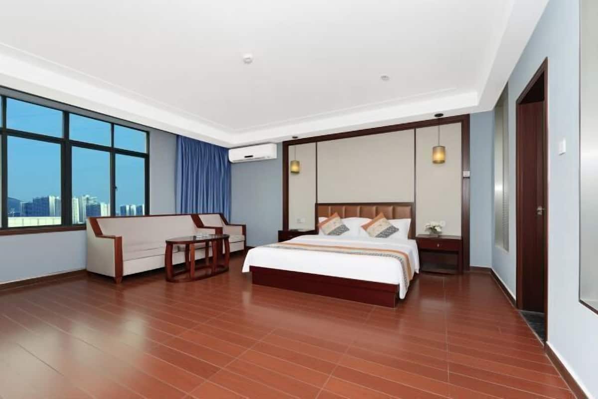 A hotel room with a large bed, a sofa, a small table, and a nightstand.