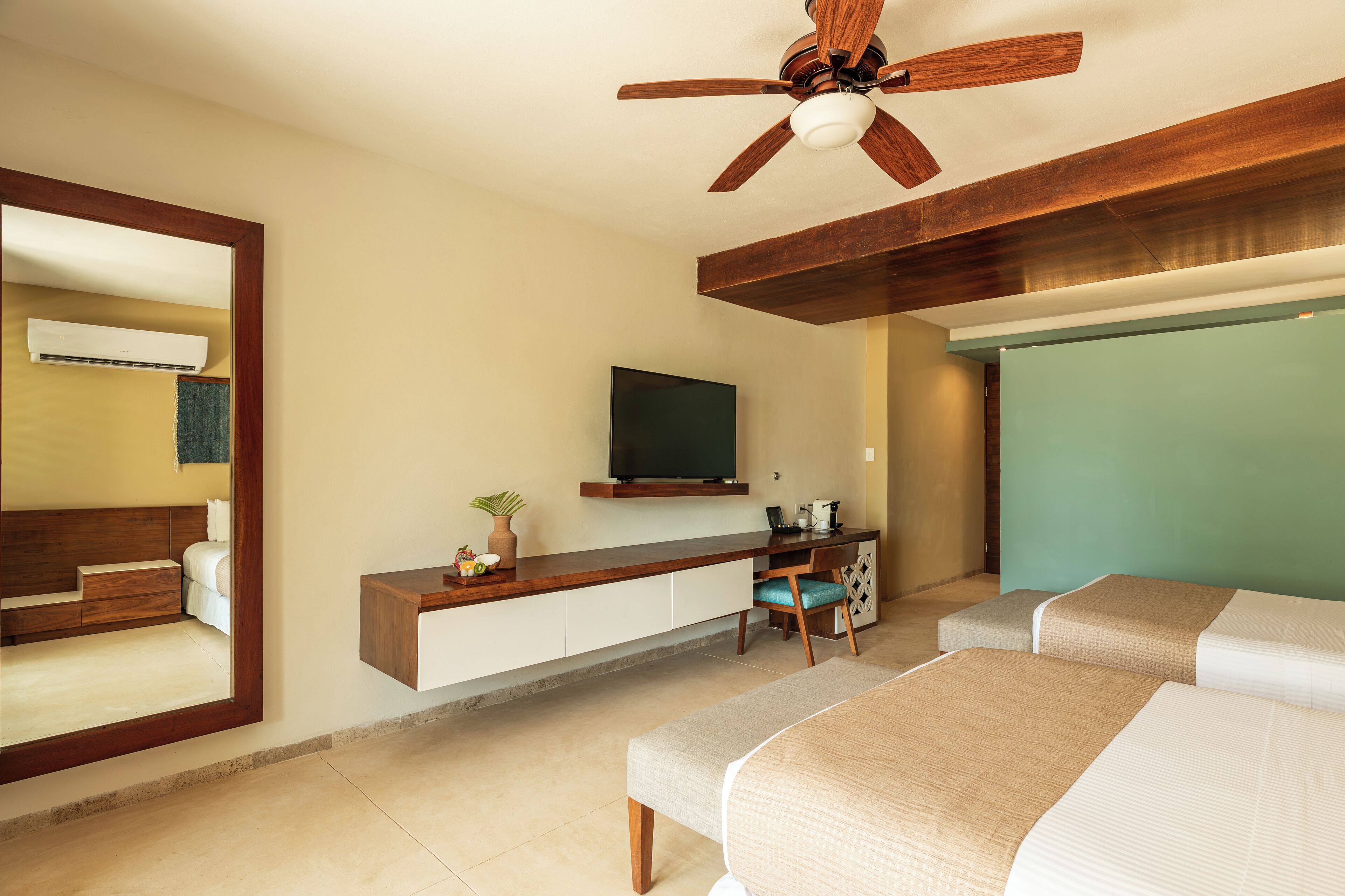 A modern hotel room with a large bed, a desk with a chair, a television mounted on the wall, and a ceiling fan.