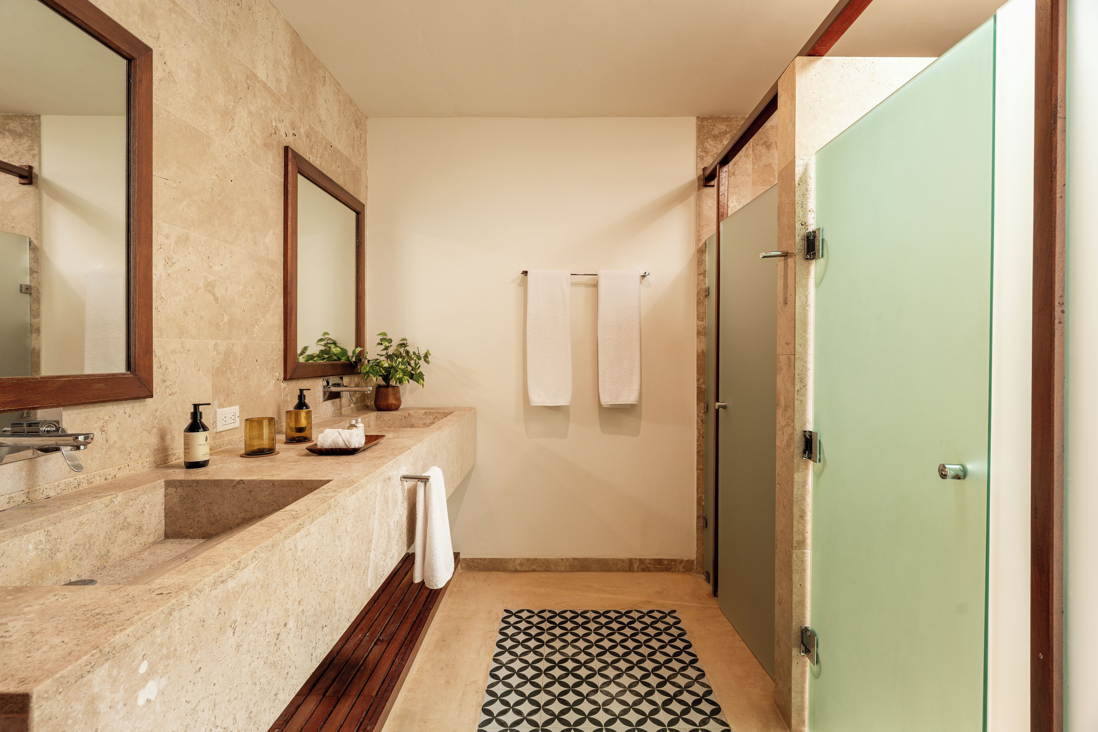Un baño con encimera de mármol color crema, alfombra de baño de madera, puerta verde y espejo.