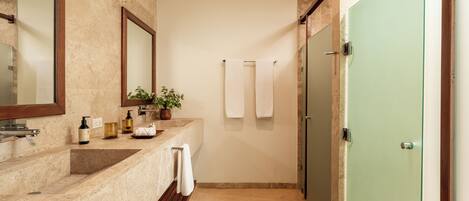 Un baño con encimera de mármol color crema, alfombra de baño de madera, puerta verde y espejo.