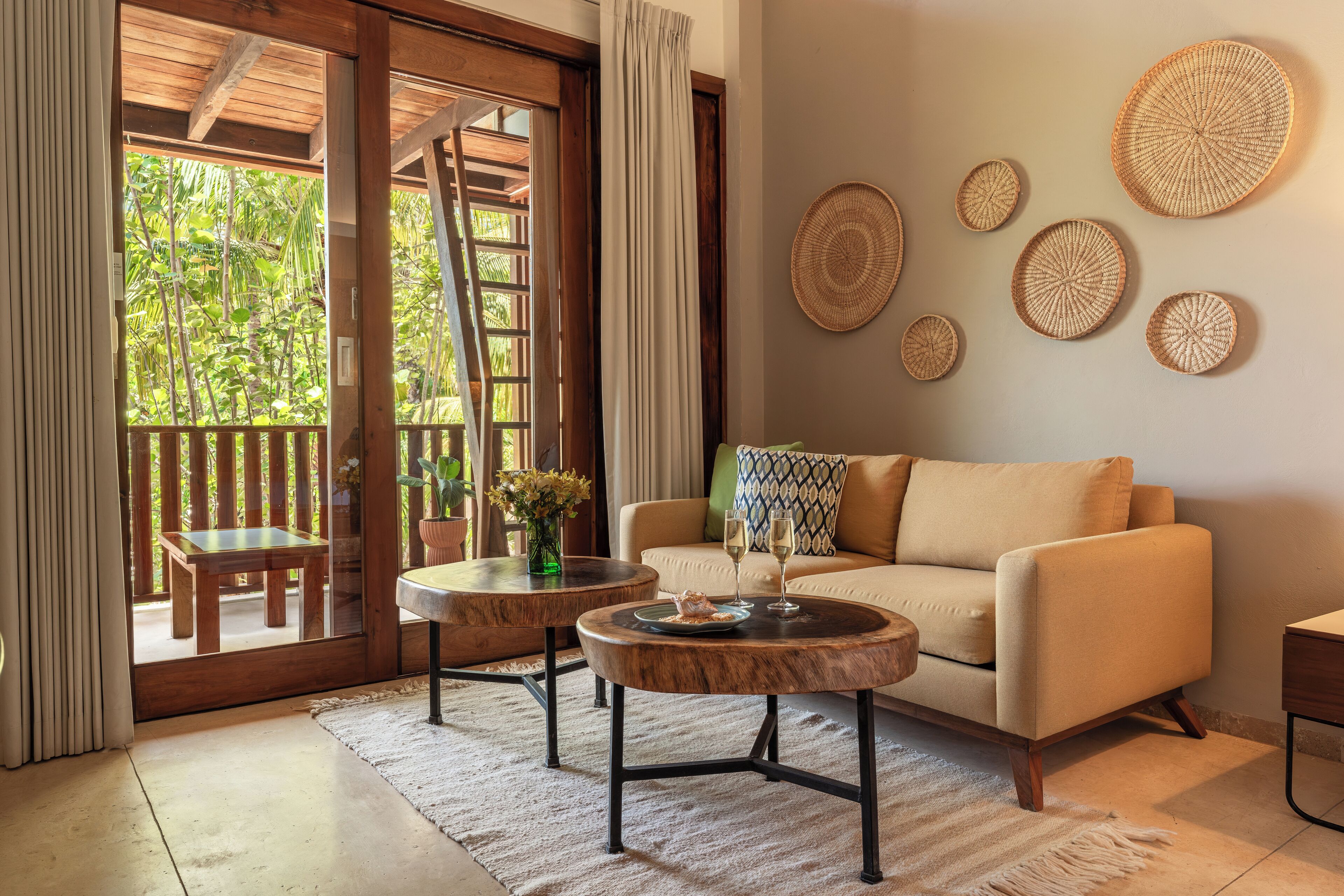 A cozy living area with a sofa, two round coffee tables, and a view of a wooden deck and greenery outside.