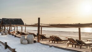 A beachside lounge with wooden lounge chairs and a thatched-roof structure. - Hotel Villas Caracol (Isla Holbox)