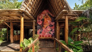 A wooden structure with a thatched roof and a mural of a woman surrounded by flowers. - Hotel Villas Caracol (Isla Holbox)