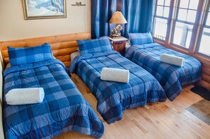 Habitación con tres camas, cada una con ropa de cama azul y toallas blancas. Tiene un cabecero de madera, una mesita de noche con lámpara y un cuadro en la pared.