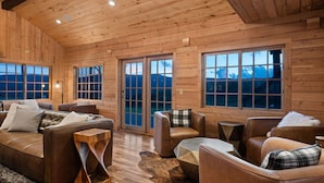 Ein rustikales Blockhaus-Interieur mit Ledersofas, Holztischen und großen Fenstern mit Blick auf die Berge.