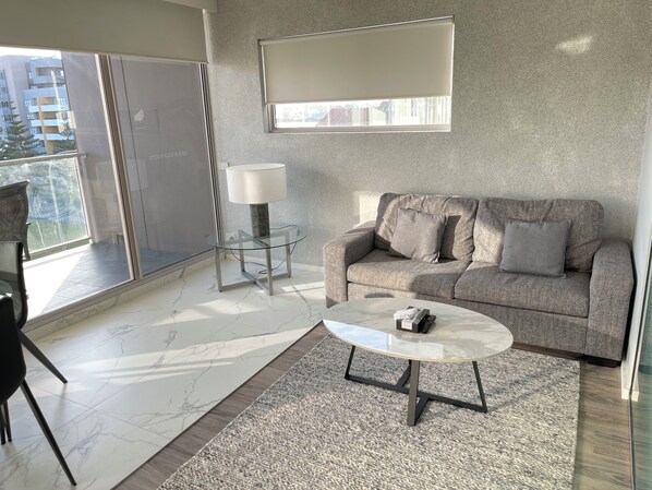 Ein modernes Wohnzimmer mit einer Couch, einem Glastisch, einer Lampe und Blick auf einen Balkon.