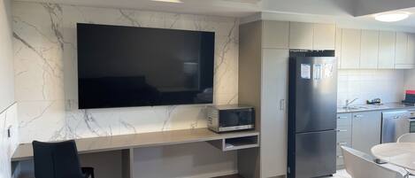 A modern kitchen with a marble backsplash, a flat-screen TV, a microwave, a refrigerator, and a dining area with chairs.