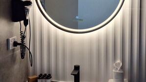 A bathroom with a round mirror, a hairdryer, a sink, and toiletries. - Prestige One Bedroom (Newcastle)