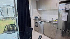 A modern kitchen with stainless steel appliances, a glass dining table, and a view of the outdoors. - Prestige One Bedroom (Newcastle)