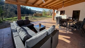 An outdoor patio with a wooden ceiling, a sofa, a dining table, and chairs.