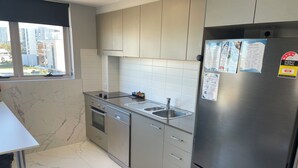 A modern kitchen with a stainless steel refrigerator, built-in oven, and dishwasher. There is a window providing a view of the cityscape.