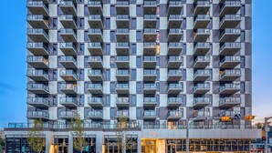 Un edificio moderno de gran altura con varios balcones, entrada a nivel de calle y cielo despejado.