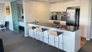 A modern kitchen with a central island, stainless steel appliances, and bar stools. - Standard Two Bedroom (Newcastle)
