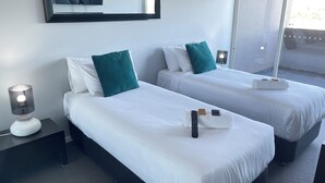 A hotel room with two beds, a large mirror, a bedside lamp, and a window with a view. - Standard Two Bedroom (Newcastle)