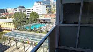 Ein Balkon mit Glasbrüstung, der einen Pool und umliegende Gebäude überblickt.