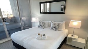 A hotel room with a large bed, two bedside lamps, a mirror, and a view of the outside. - Prestige Two Bedroom (Newcastle)
