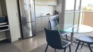 A modern kitchen with stainless steel appliances, a glass dining table, and a view of the city through large windows.