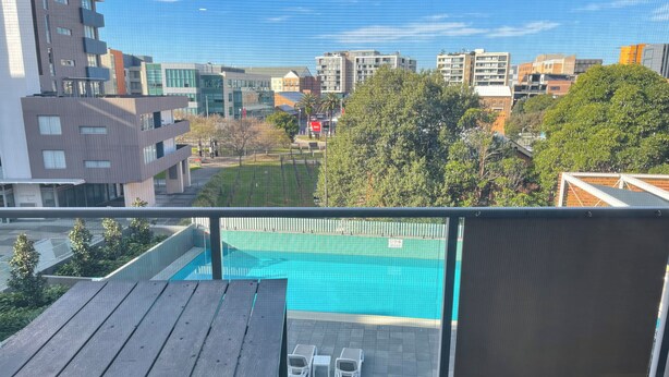 En balkon med udsigt til en swimmingpool, moderne bygninger og en græsplæne.